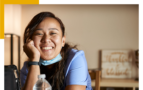 Woman smiling wearing scrubs and a medical mask